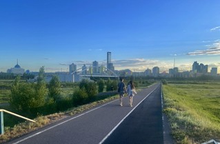 6月29日，人们在哈萨克斯坦首都阿斯塔纳一处公园内散步，远处是阿斯塔纳城市天际线。（图片来源：新华社）