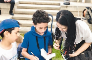 　今年端午节，刘津巧(右)在当地的龙舟赛活动中为外国小朋友介绍中国书法。