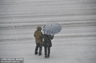 12月11日，行人在山东省烟台市福山区永安街冒雪出行。