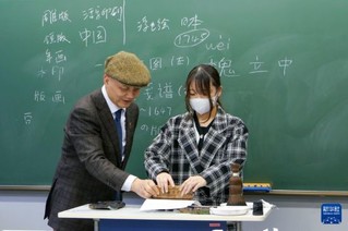 12月19日，在日本东京都的中央大学，木版水印传承人、浙江十竹斋版画博物馆馆长魏立中（左）指导一名大学生体验木版水印技艺。新华社发