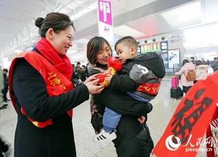 “小朋友，今年是狗年，送你一个玩具小狗，祝你一路平安，路上要听爸爸妈妈的话哦！”上海虹桥心尚雷锋服务站的客运员邵玮（左一）和同事为小旅客送上玩具小狗和福字，祝福旅客一路平安。