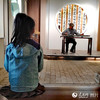 在西河古镇弋農古琴斫制工艺馆内，一位小朋友正在全神贯注地聆听弋農古琴非物质文化遗产代表性传承人翟光宝弹奏的古琴曲。翟光宝是弋農古琴斫制工艺的第四代传承人。弋農古琴又称“百纳琴”，是以古木片合漆胶合而成的琴，始创于唐代。