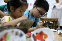 7月13日，在浙江湖州南浔的荻港古村，小朋友在蚌壳上作画。新华社发（吴建勋摄）